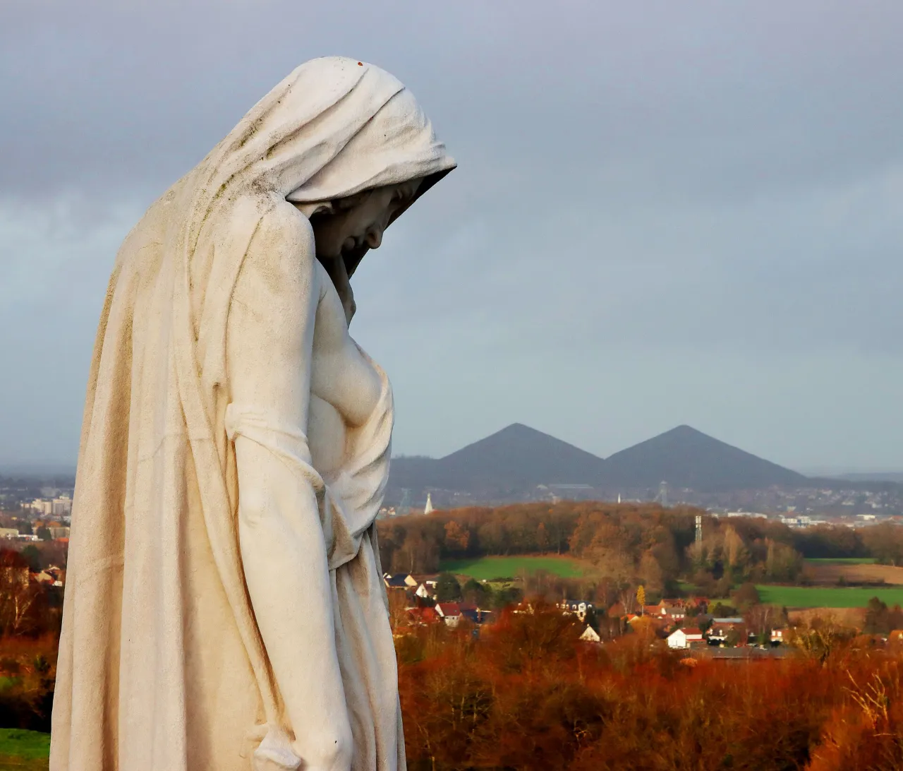 La statue voilée du Canada en deuil tournée vers la plaine, avec les terrils jumeaux à l’horizon
